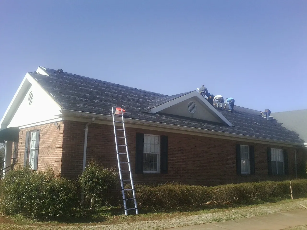 Crew tearing shingles off a brick ranch roof with a ladder set — Emergency Roof Repair work by our crew in Huntland