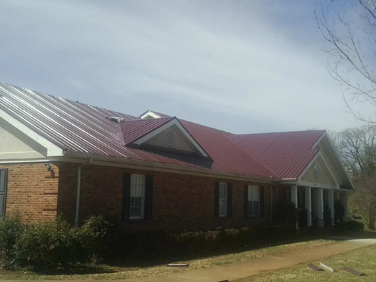 Red metal roof with gabled entries on a long brick building, from a Hail Damage Roof Repair job in Huntland