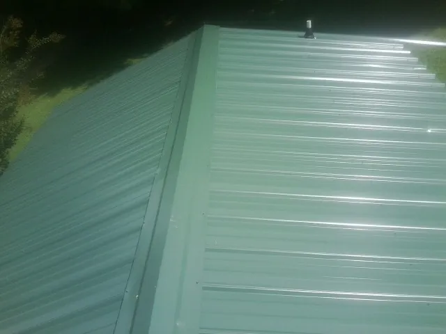 New green metal panels meeting at the ridge of a roof — Flat Roof Repair work by our crew in Huntland