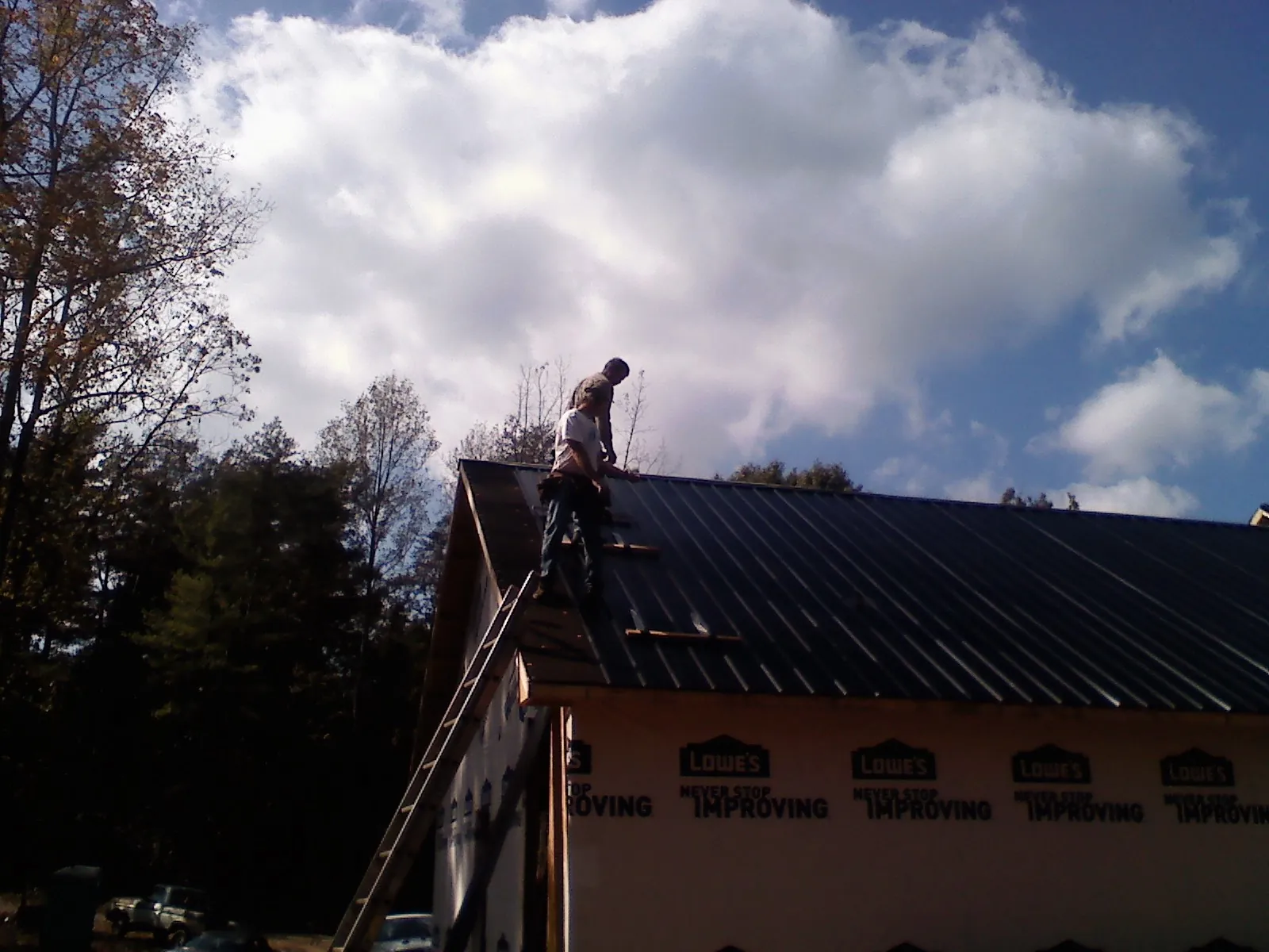 Roofer fastening dark metal panels high against a cloudy sky, from a Roof Inspection job in Huntland