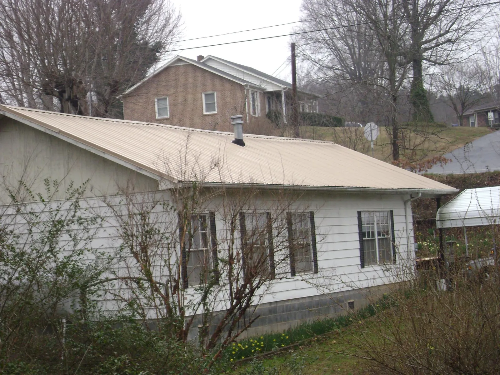 Tan metal roof on a white sided house set into a hillside — Commercial Roofing by Roofing Brothers in Huntland