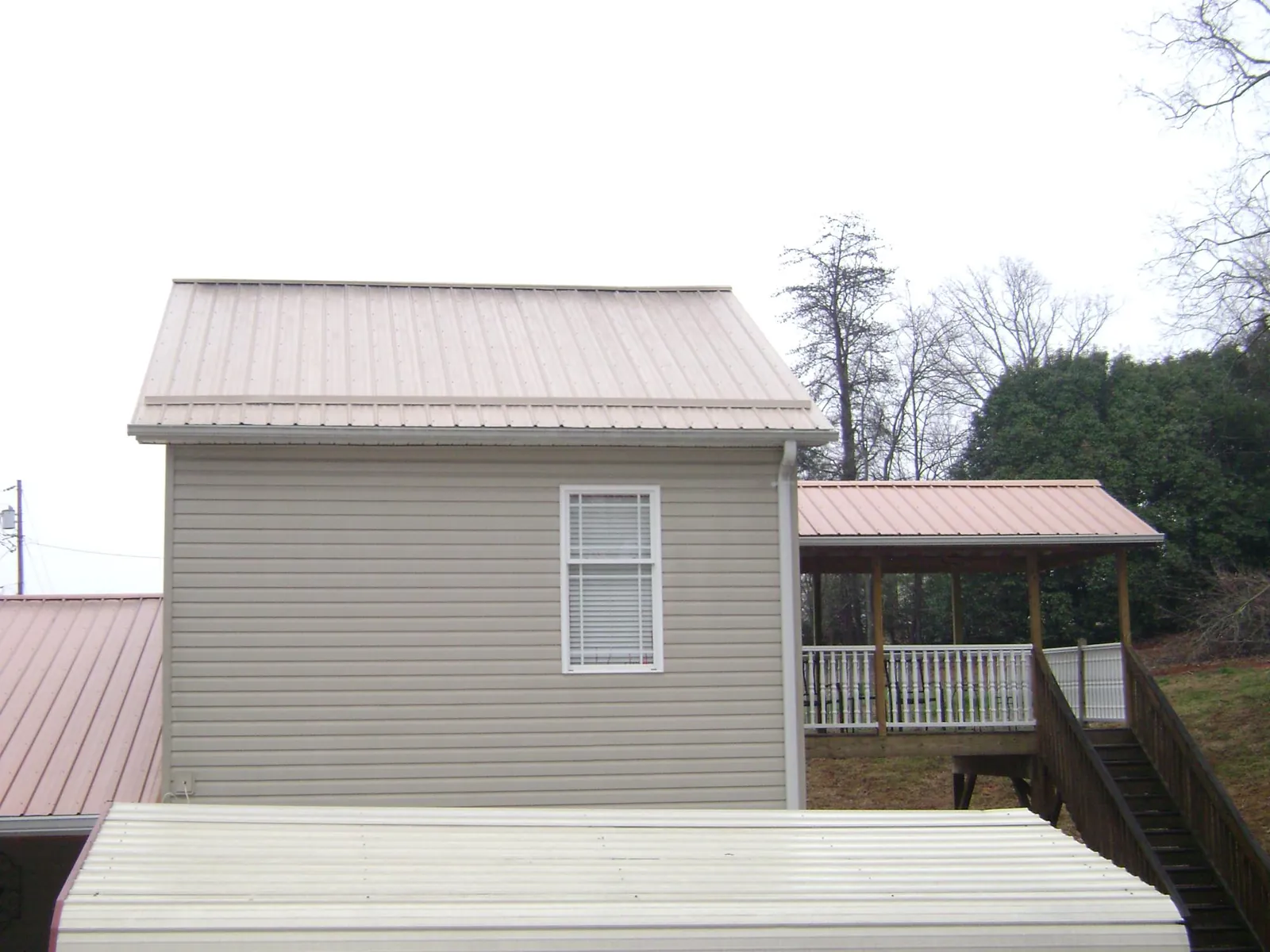 Tan metal roofs on a two story addition and attached porch, from a Roof Replacement job in Huntland